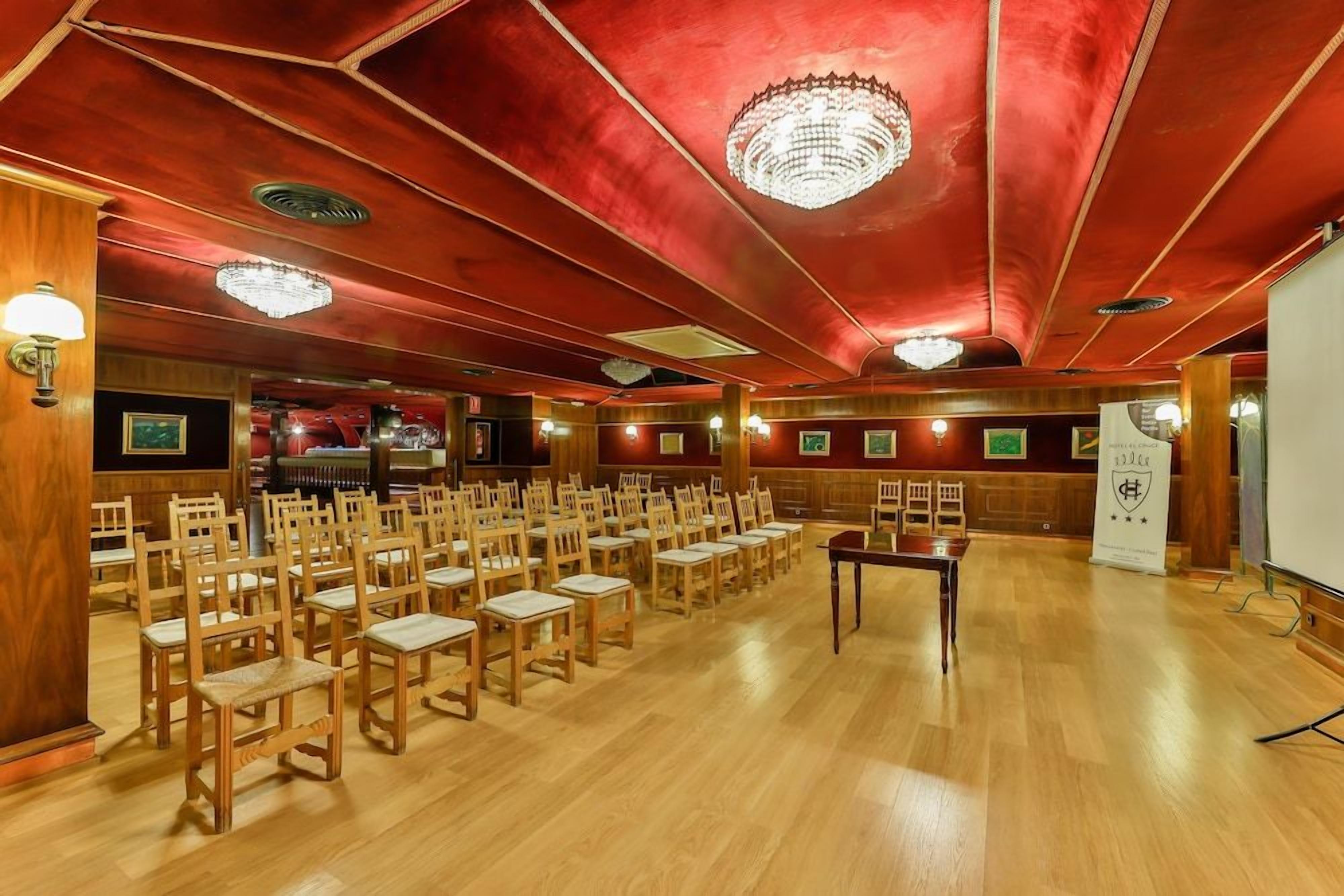 Un salón de conferencias con filas de sillas de madera, una pantalla de proyector y un atril.