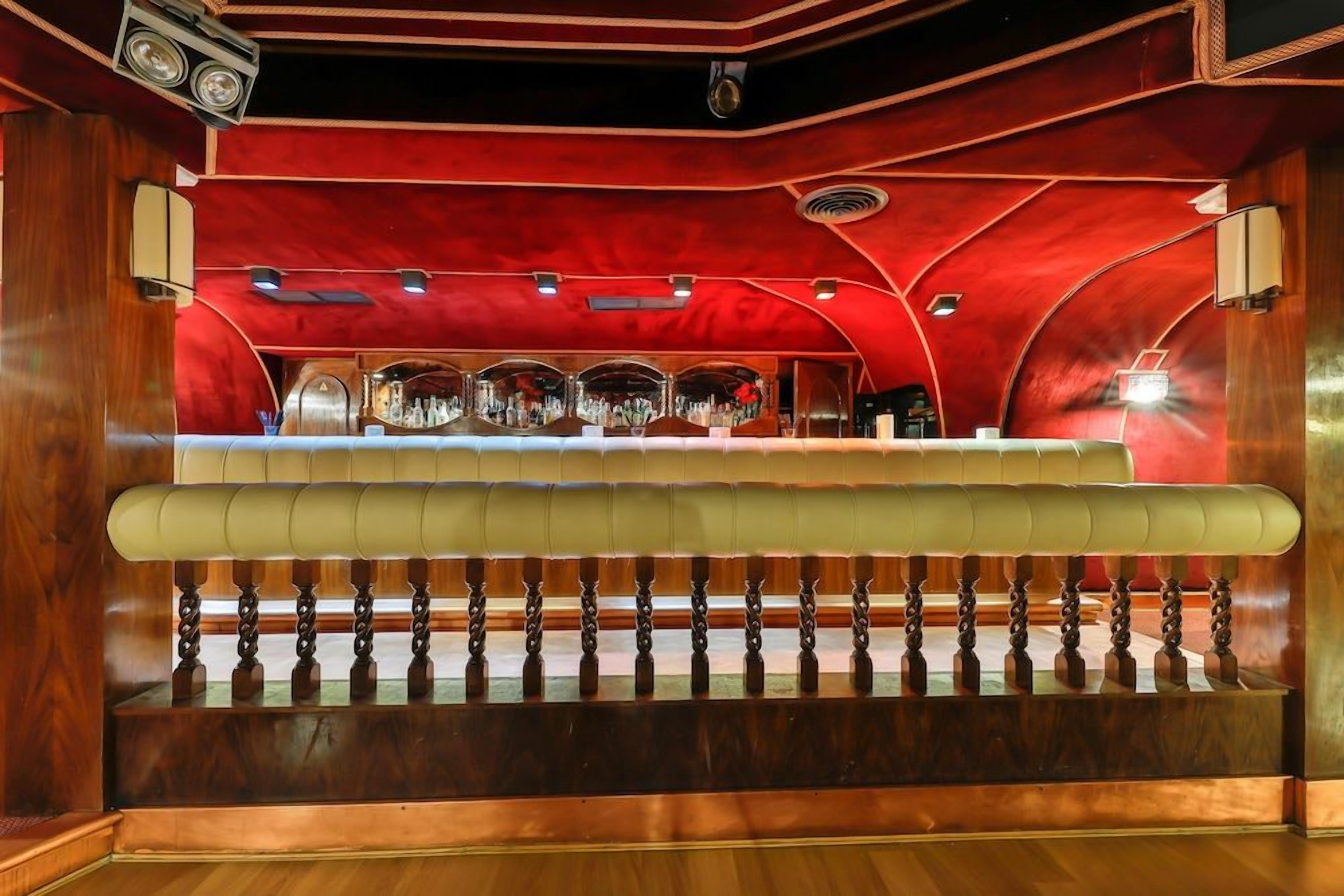 Una zona de bar con mostrador, asientos acolchados y techo rojo.