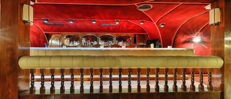 Una zona de bar con mostrador, asientos acolchados y techo rojo.