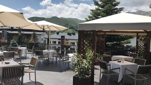 An outdoor patio area with tables and chairs, covered by large umbrellas, and surrounded by potted plants. - Villa de Sallent (Sallent de Gallego)