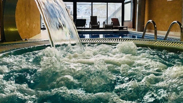 An indoor swimming pool with a waterfall feature, lounge chairs, and a view through large windows. - Villa de Sallent (Sallent de Gallego)