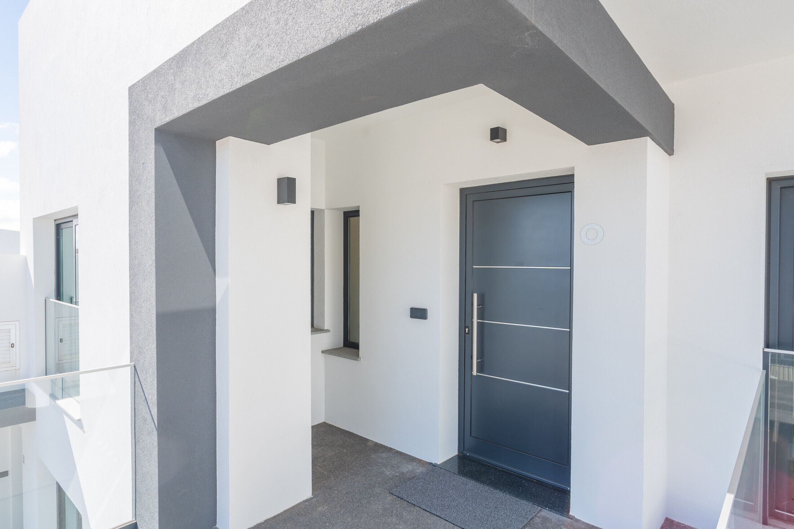 Ein modernes Gebäude mit Hauseingang, einer dunklen Tür, einem Glasbalkon und einer Betonkonstruktion.