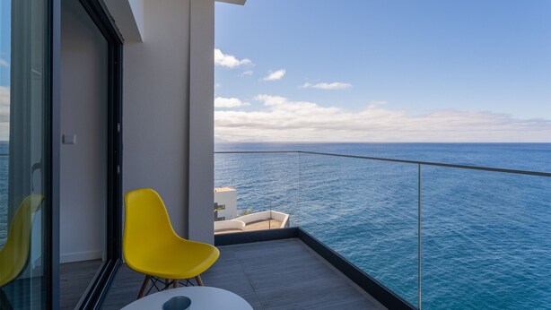 Ein Balkon mit Blick auf das Meer, eine Glastür und gelbe Stühle.