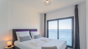 Ein modernes Hotelzimmer mit einem großen Bett, einem Nachttisch mit Lampe und Meerblick durch ein großes Fenster.