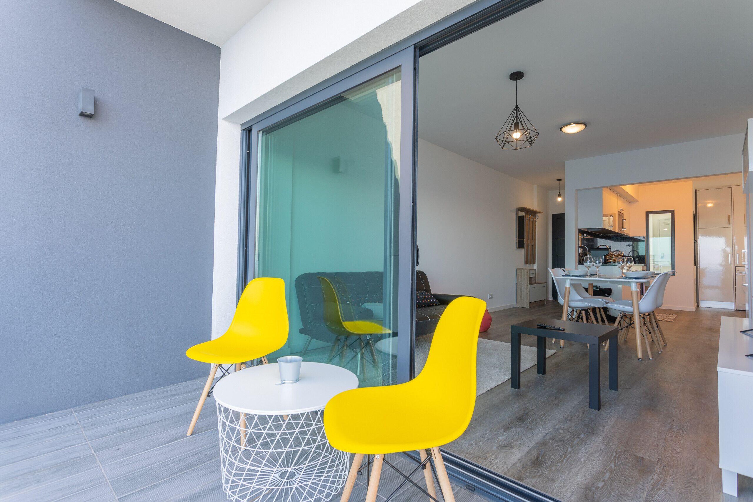 A modern dining area with a glass partition, a round table, and yellow chairs.