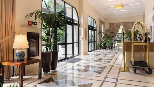 Un hall d’hôtel avec un comptoir d’enregistrement, des plantes en pot, une grande fenêtre et un sol carrelé.