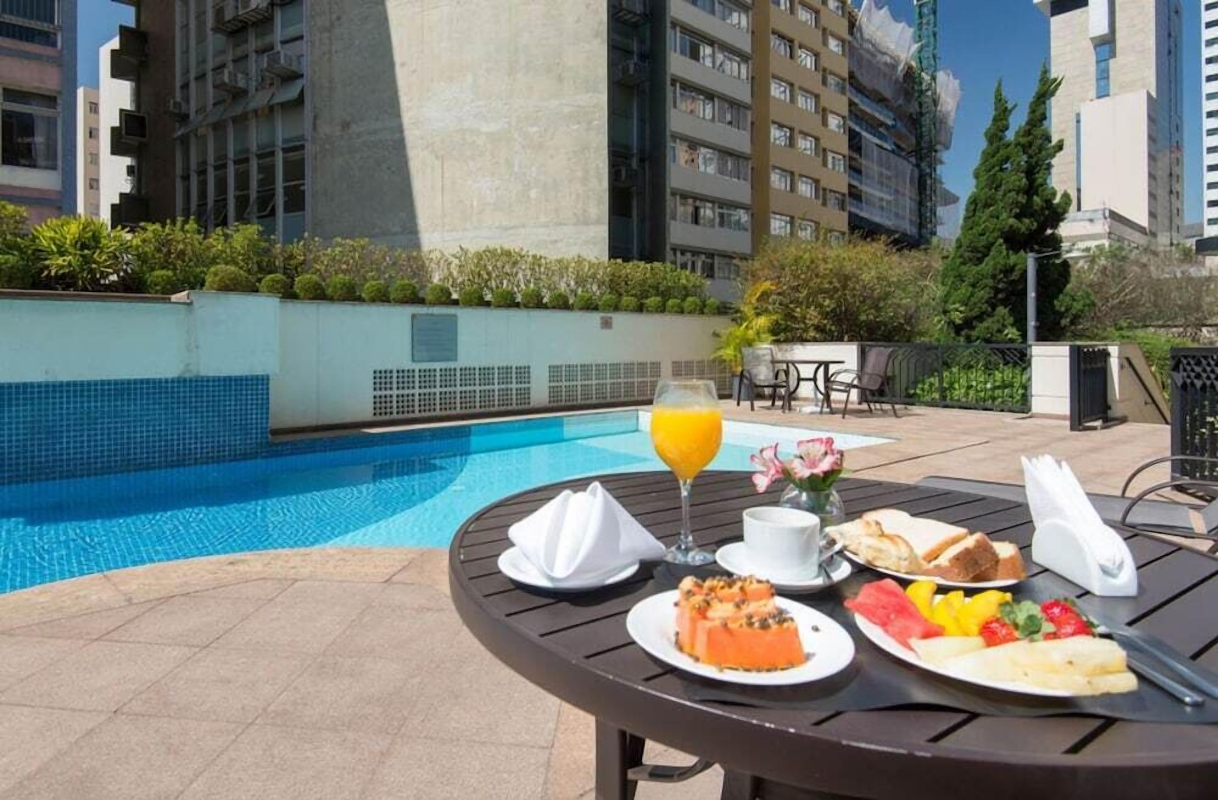 Mesa de jantar com itens de café da manhã e um copo de suco de laranja perto de uma piscina.