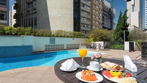 Une table à manger avec des aliments pour le petit-déjeuner et un verre de jus d’orange, le tout placé près d’une piscine.