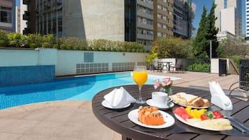 Mesa de jantar com itens de café da manhã e um copo de suco de laranja perto de uma piscina.