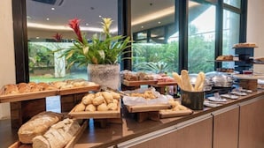 Un buffet de petit-déjeuner proposant une variété de pains et de viennoiseries, une plante en pot et une vue sur la verdure grâce à de grandes fenêtres.