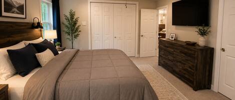 A bedroom with a bed, a ceiling fan, a dresser, a TV, and a door.
