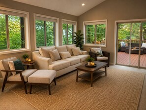 Ein Wohnzimmer mit einem beigefarbenen Sofa, einem Holztisch und einem großen Fenster mit Blick auf Grünflächen.