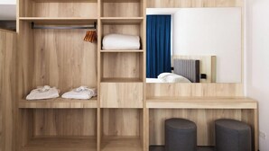 A modern room with a wooden wardrobe, a mirror, a desk, and two ottomans.