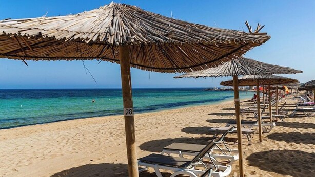 A beach with thatched umbrellas and sun loungers.