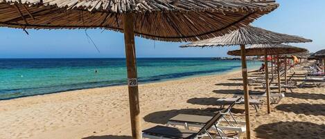 Una playa con sombrillas de paja y tumbonas.