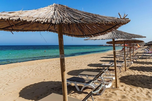 A beach with thatched umbrellas and sun loungers.