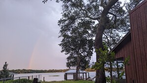 Blick auf einen See mit einem Holzbauten, einem Pavillon und einem Regenbogen.