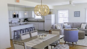 A spacious living area with a dining table, chairs, and a sofa. There is a kitchen area with a microwave, stove, and bar stools. An exit sign is visible on the wall.