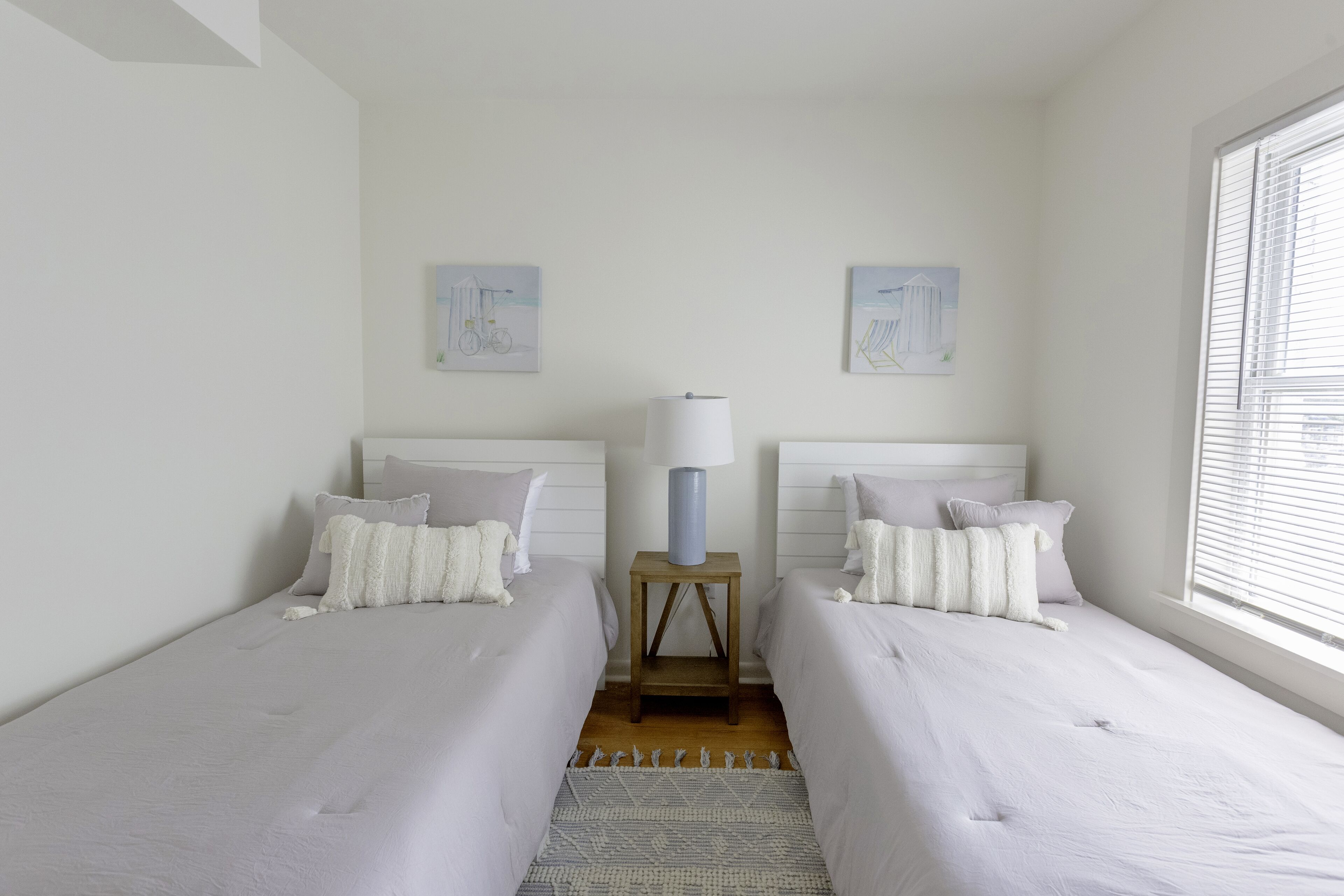 A bedroom with two beds, a nightstand with a lamp, and artwork on the walls.
