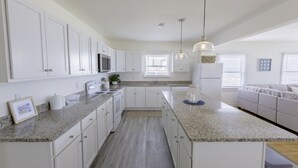 A modern kitchen with white cabinets, granite countertops, a built-in microwave, and a large island with a sink.