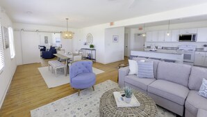 A spacious living room with a grey sofa, a blue armchair, and a dining area with a white table and chairs.