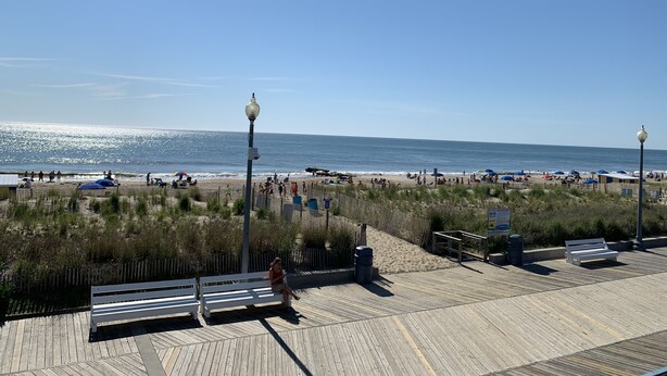 A beach with a wooden boardwalk, benches, and a fence.