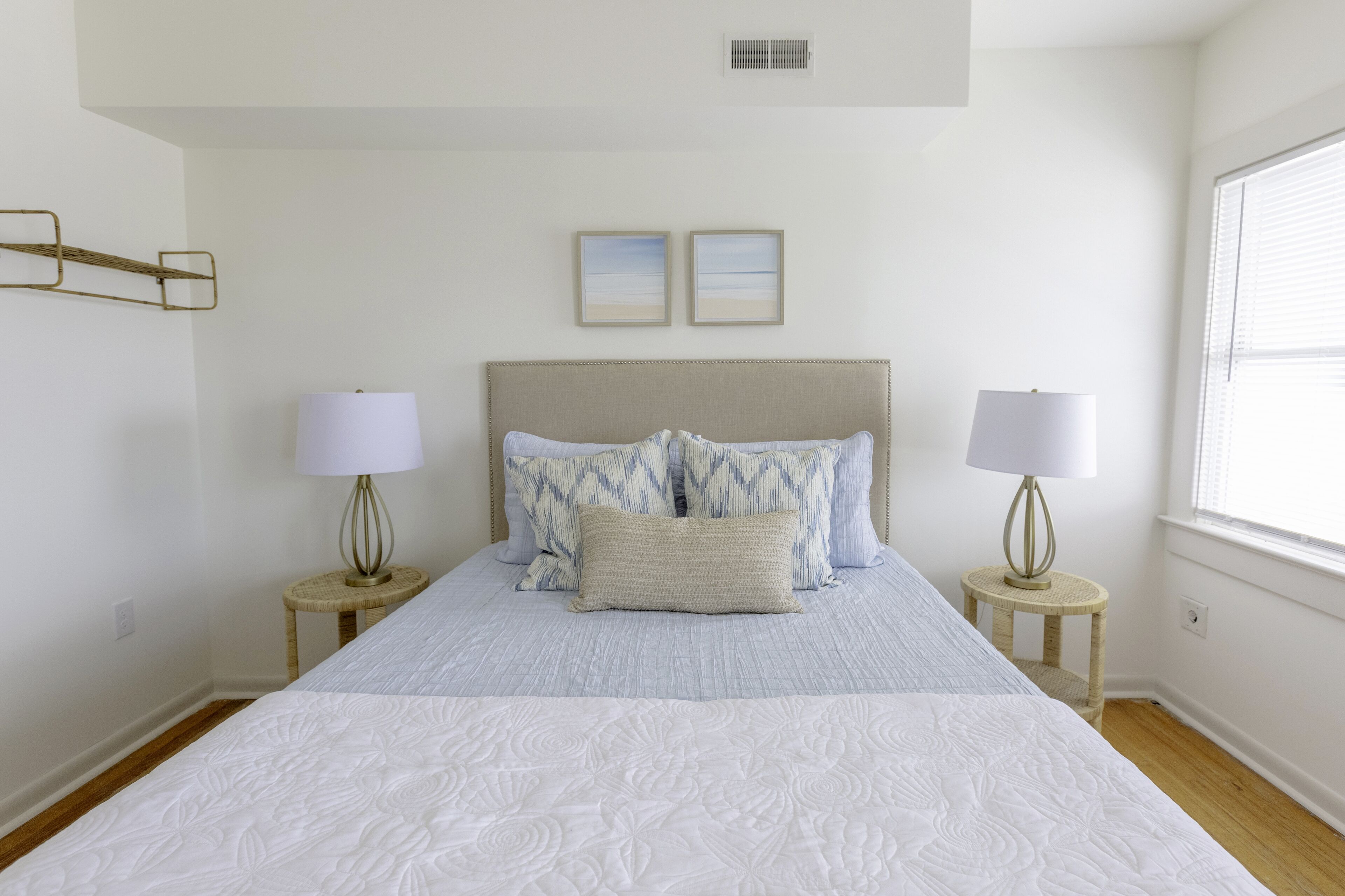 A bedroom with a large bed, two bedside tables with lamps, a headboard, and two framed pictures on the wall.