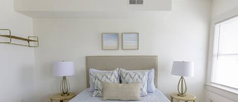 A bedroom with a large bed, two bedside tables with lamps, a headboard, and two framed pictures on the wall.