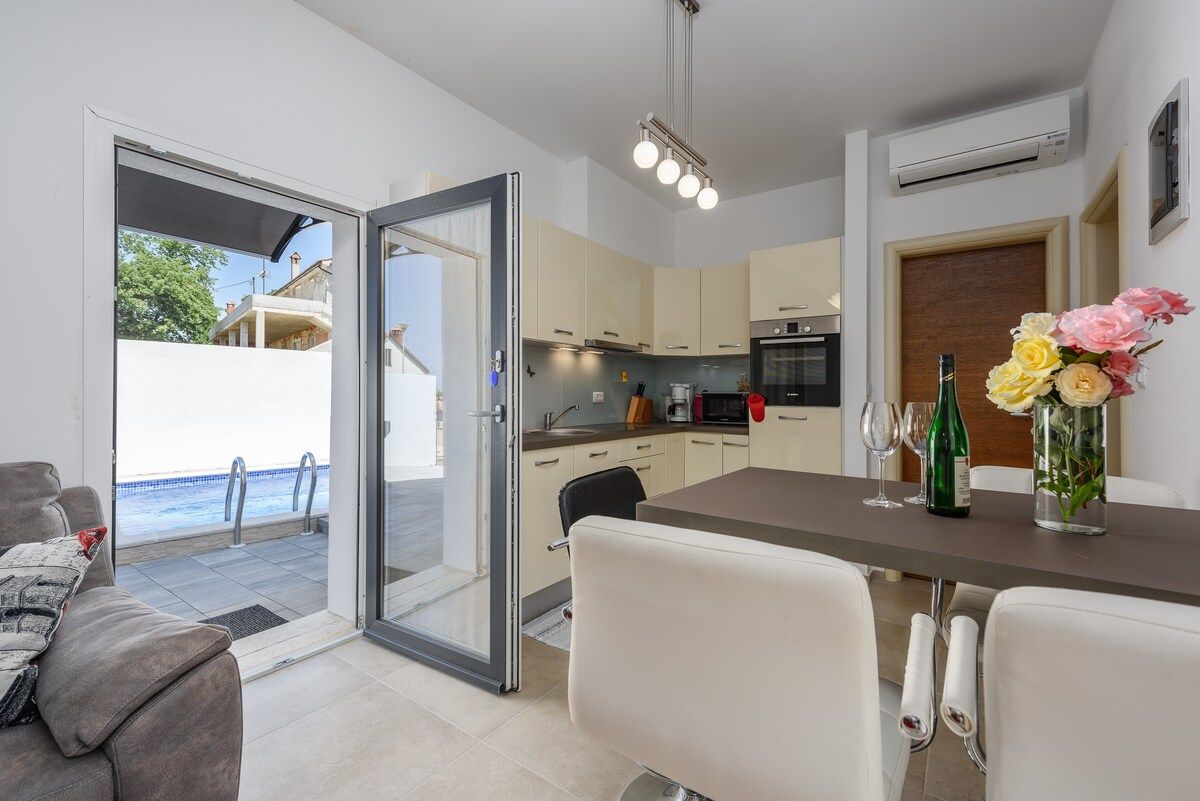 A modern kitchen with a dining area, a sliding glass door leading to a balcony, and a vase of flowers on the table.