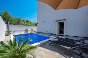 Un espace piscine avec une piscine à l’eau cristalline, des chaises longues et une porte donnant sur un patio abrité.