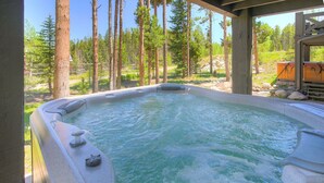 A hot tub in a natural setting with a wooden deck and a view of a forest.