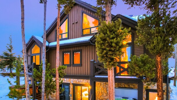 A multi-story lodge with a stone facade, large windows, and a hot tub in the foreground.