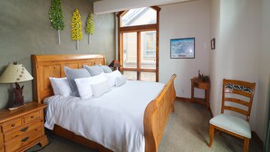 A bedroom with a wooden bed, a nightstand, a chair, and a window with blinds.