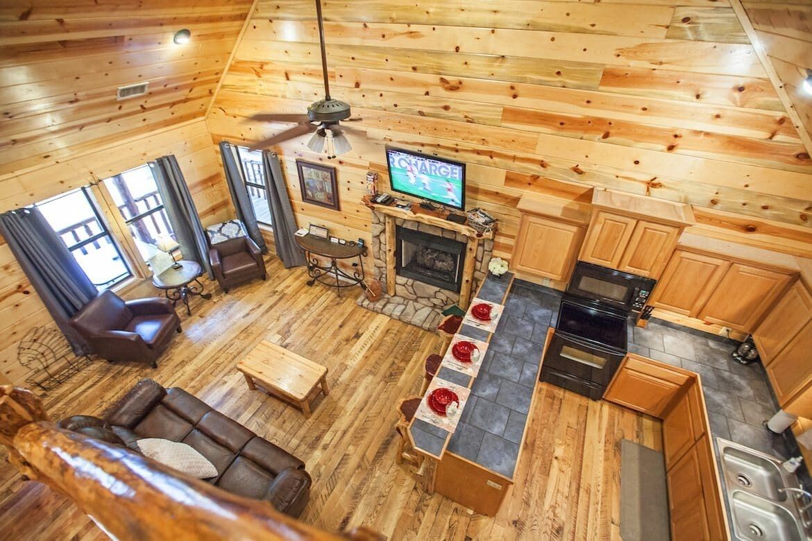 A cabin interior with a living room, dining area, fireplace, kitchen, and a television displaying a sports game.
