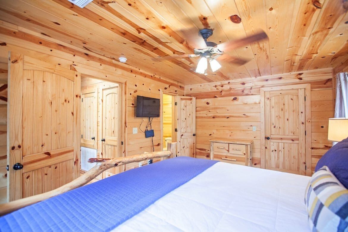 Une chambre rustique en bois, avec un lit, un ventilateur de plafond et un téléviseur fixé au mur.