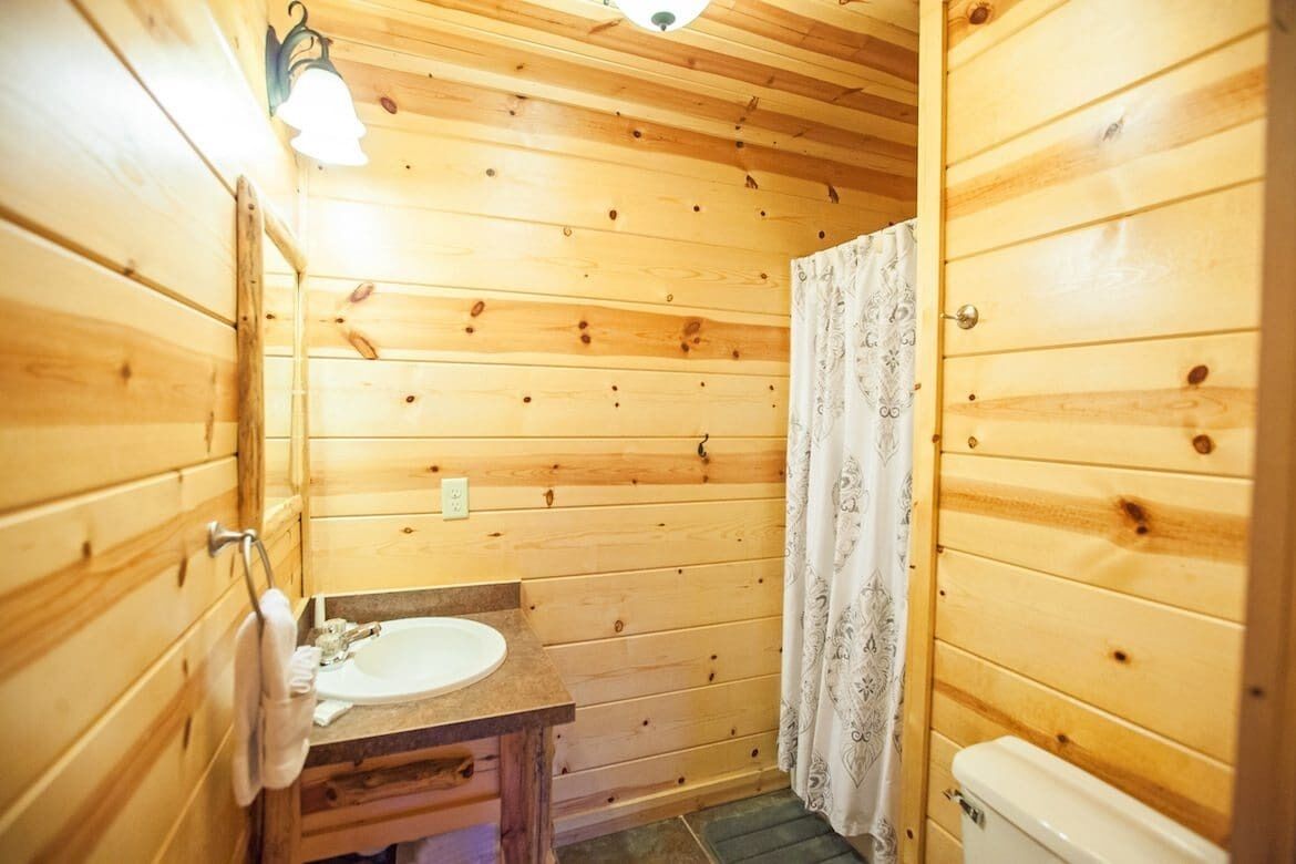 A wooden cabin bathroom with a sink, toilet, and shower curtain.