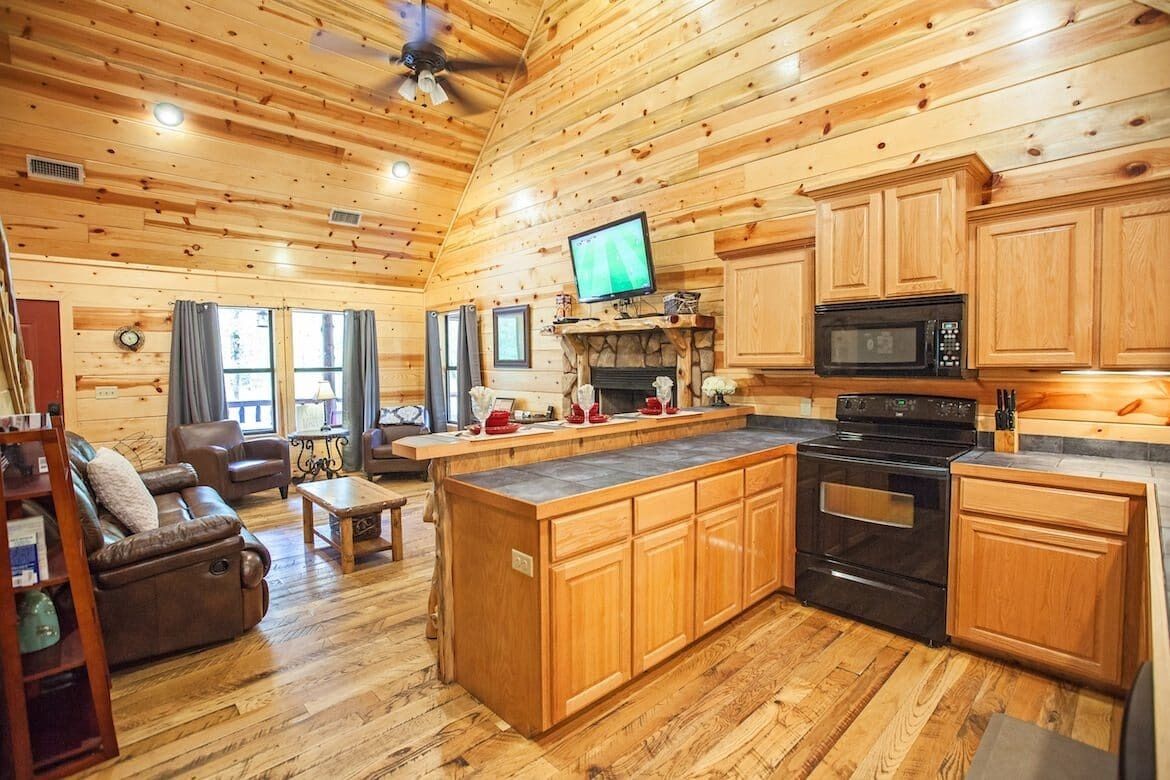 A cabin interior with a wooden interior, a fireplace, a kitchen with a microwave, and a television.