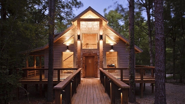 Une cabane en bois avec une porte centrale, deux fenêtres de chaque côté et une terrasse en bois menant à l’entrée.