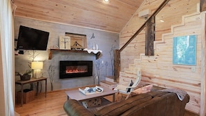 Un salon chaleureux avec une cheminée, des murs en bois, un téléviseur et un escalier.