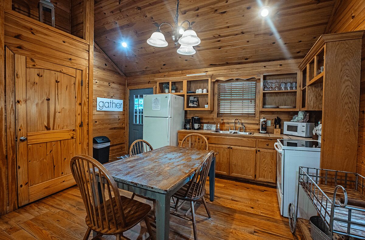 A rustic kitchen with wooden cabinets, a dining table, and a refrigerator.