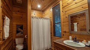 A wooden cabin bathroom with a toilet, shower curtain, sink, and a mirror.