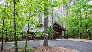 Une cabane dotée d’un porche, entourée d’arbres et accessible par une allée pavée.