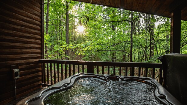 Un bain à remous avec une terrasse en bois et une vue sur une forêt.