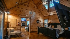 Une chambre située dans une cabane en rondins, avec un plancher en bois, un lit, une chaise, un téléviseur et une cheminée.