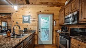 Une cuisine rustique, située dans une cabane en bois, avec des comptoirs en granit, des appareils électroménagers en acier inoxydable et une porte dotée d’une fenêtre.