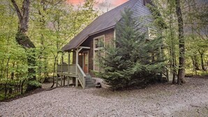 Une cabane dotée d’une terrasse en bois, entourée d’arbres et bordée d’un chemin de gravier.