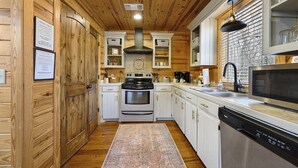 Une cuisine compacte avec des murs en bois, des armoires blanches, une cuisinière, un four, un four à micro-ondes et un lave-vaisselle.