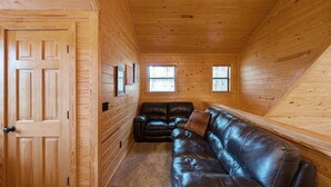 Ein Holzblockhaus-Interieur mit einer Holztür, einem Ledersofa und zwei Fenstern.
