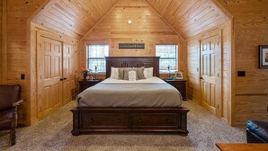 Ein gemütliches Schlafzimmer mit Holzbalkendecke, einem großen Bett, zwei Nachttischen und einem Sessel.