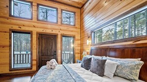 A log cabin bedroom with a large bed, multiple windows, and a view of trees. - Journeys End -2 BR-Timber Creek Trails (Broken Bow)